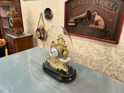 Antique French 1890s glass-domed marquetry fireplace clock displayed on a table in a vintage-themed room.