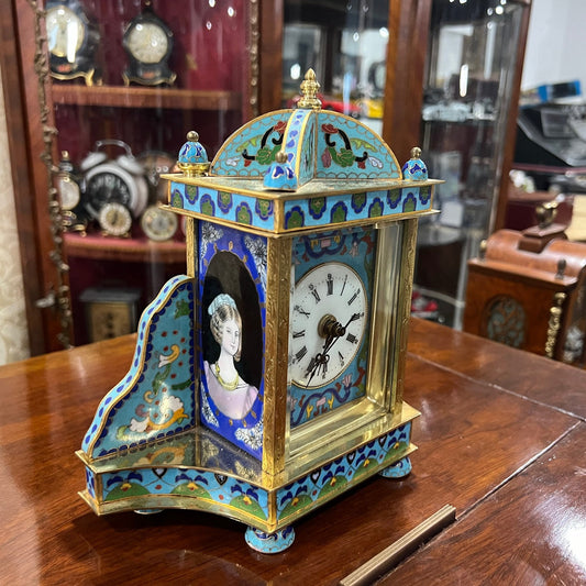 Collectible antique enamel brass quartz clock with intricate design on display in a cabinet
