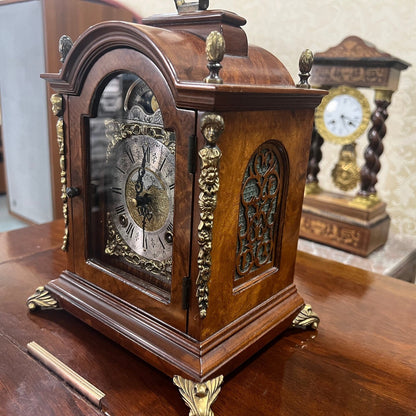 Antique Hermle double wind wood mantel clock with intricate gold details and elegant design displayed on wooden surface.