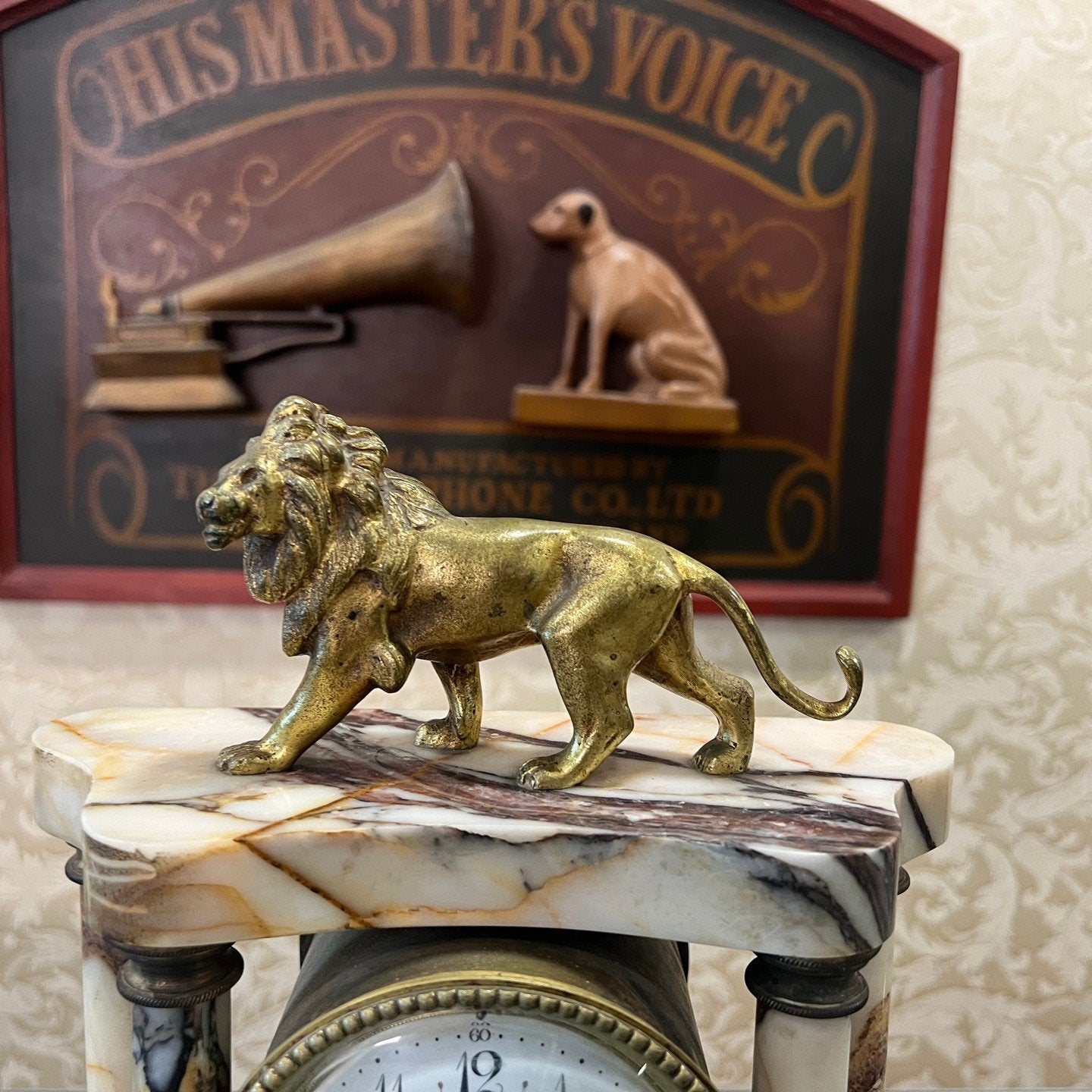 Antique French mantel clock with marble base and brass lion figurine, His Master's Voice sign in background